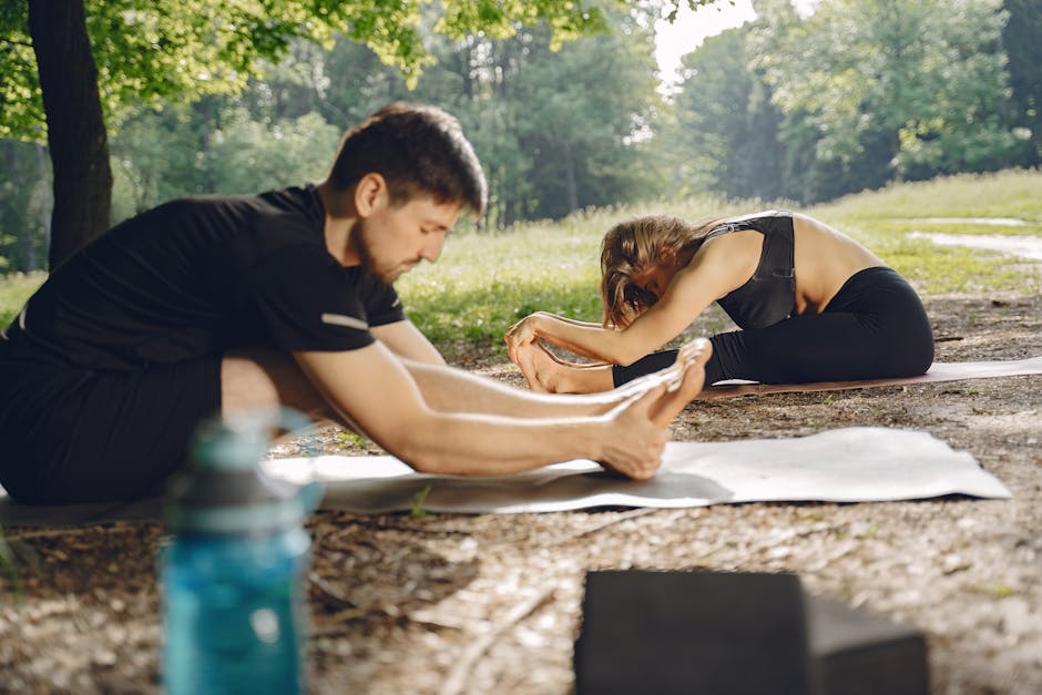 A man and woman practicing yoga outdoors in a sunny park, focusing on stretching.